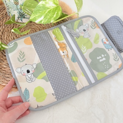 Carteira ou organizador de tecido com padrão de animais e folhas em verde, cinza e bege.