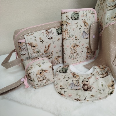 Conjunto de acessórios para bebé com padrão de coelhos vestidos em cores bege, rosa e verde claro sobre tecido macio.