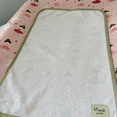 toalha de bebé branca com borda verde e padrão azul sobre superfície rosa com bailarinas e cisnes
