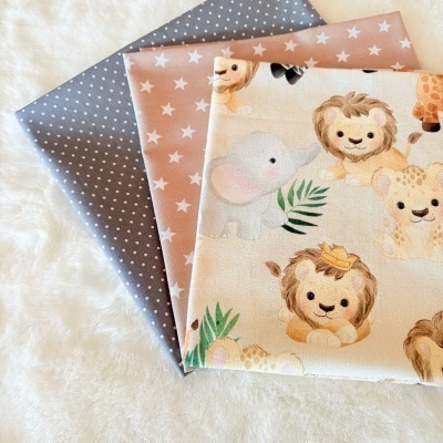 Três tecidos coloridos com padrões de bolinhas, estrelas e animais bebés sobre superfície branca felpuda.