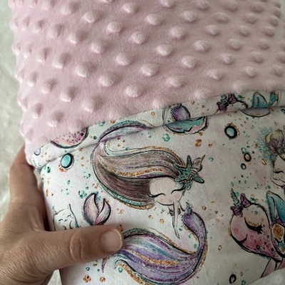 Almofada rosa com textura de bolinhas e lado estampado com sereias e peixes