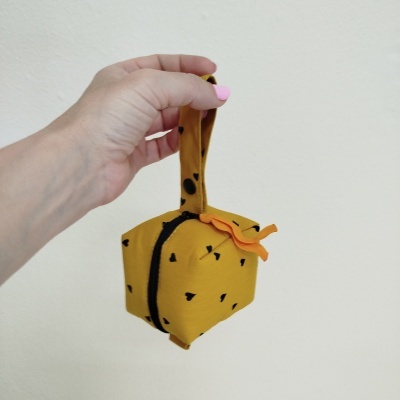 Bolsa pequena amarela com pintas pretas e detalhe laranja, com alça, segurada por mão