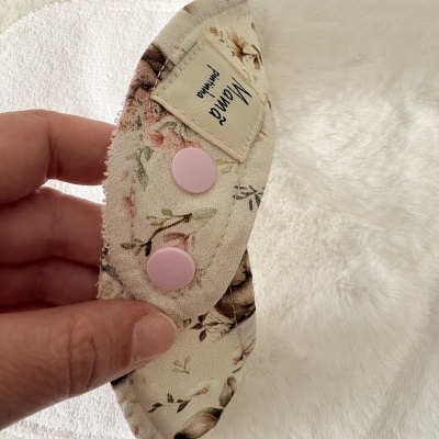 Fralda reutilizável branca com aba floral e botões rosa sendo segurada pela mão