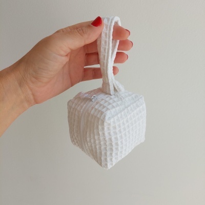Bolsa pequena branca com textura em quadrícula segurada por mão com unhas vermelhas