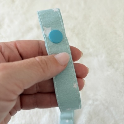 Cinta de tecido azul claro com padrão de estrelas brancas e botão azul numa mão