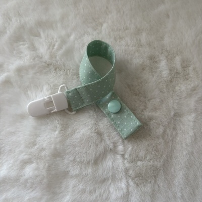 Clips de chupeta verde menta com pontos brancos sobre tecido felpudo branco