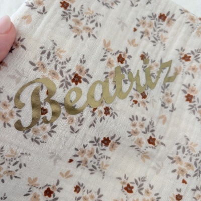 Tecido branco com flores castanhas e bege e texto dourado
