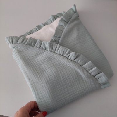 Fralda de algodão verde-água com folhos e textura amassada, segurada por uma mão.