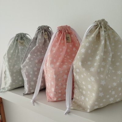 Quatro sacos de tecido coloridos com estrelas brancas e cordões brancos em superfície branca