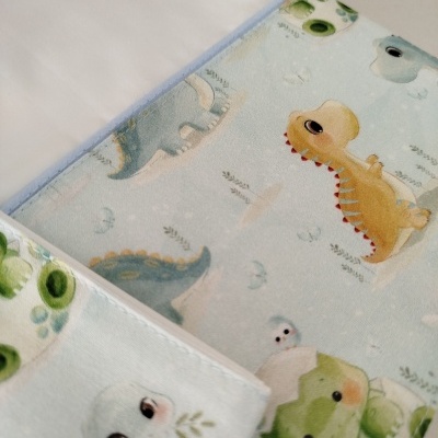 Tecido branco com padrão infantil de dinossauros coloridos em fundo azul claro