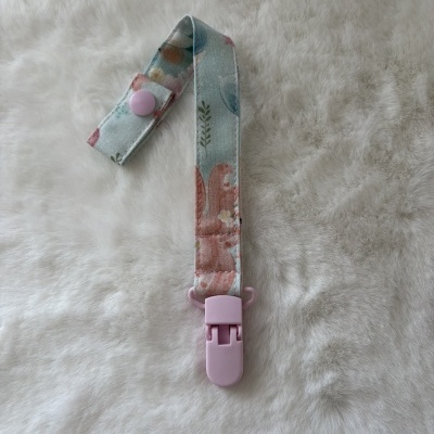 Tira com clip de plástico rosa e tecido estampado floral sobre superfície branca felpuda