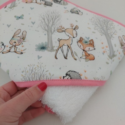 Toalha de bebé com tecido branco, borda com ilustrações de animais e costura rosa