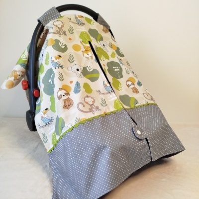 Capa protetora para cadeirinha de bebé, padrão animais e folhas, base cinza com bolinhas brancas.