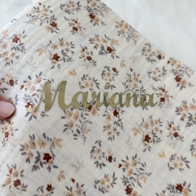 Pano branco com padrão floral castanho e bege e nome Mariana em letras douradas