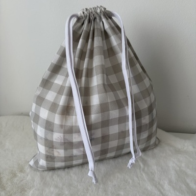Mochila de tecido quadriculada bege e branca com cordões brancos sobre superfície macia