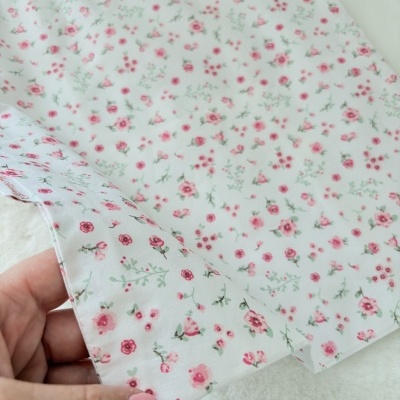 Tecido branco com padrão floral rosa e verde segurado por mão com unha pintada de rosa