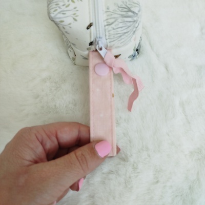 Mão segurando pega de zíper rosa com padrão de pontos na bolsa branca com padrão floral