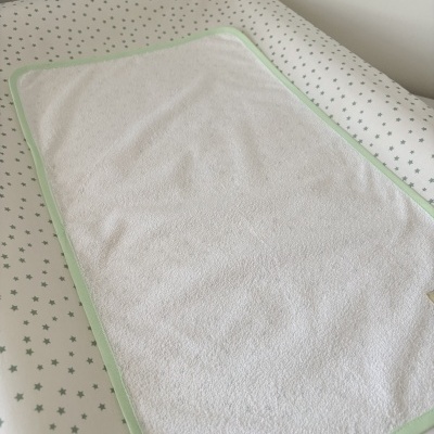 Toalha ou fralda branca com borda verde claro sobre colchão branco com estrelas verdes