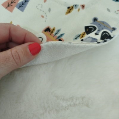 Manta branca com padrão colorido e textura felpuda, segurada por mão com unhas vermelhas