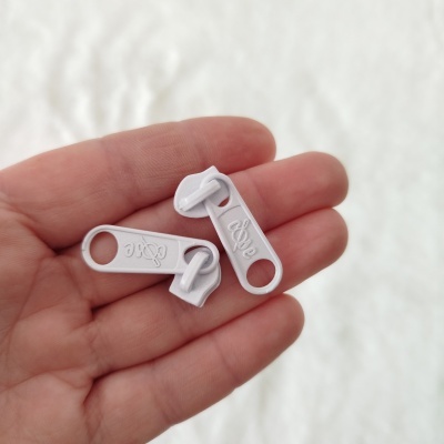 Puxadores de fecho éclair brancos em plástico com texto Opé na mão de uma pessoa.