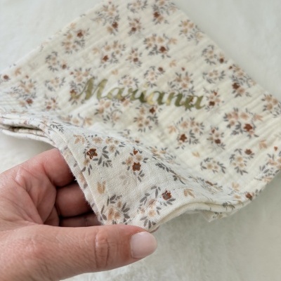 Guardanapo de tecido branco com padrão floral e nome dourado
