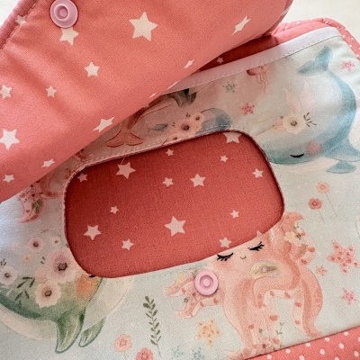 Babete de tecido rosa com estrelas e padrão de sereias e golfinhos em tons pastel.