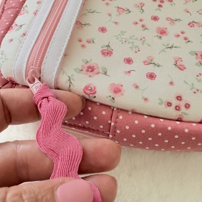 Carteira com fecho de correr rosa e padrões de flores e bolinhas em tons de rosa.