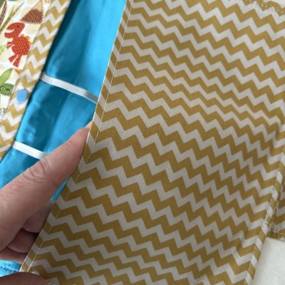Bolsa em tecido com padrão zig zag amarelo e branco, interior azul e estampa colorida de animais.