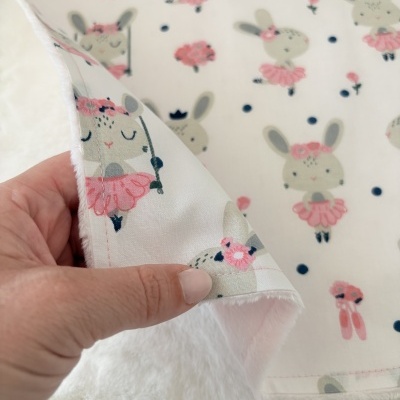tecido branco com padrão de coelhinhos vestidos em rosa segurado por uma mão