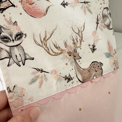 tecido com padrão de animais, flores e estrelas em tons pastel e rosa