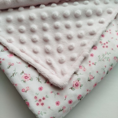 Mantas dobradas, uma rosa com bolinhas em relevo e outra branca com padrão floral rosa e verde.