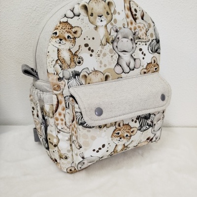 Mochila infantil bege com estampa de animais selvagens em tons castanhos e cinza.