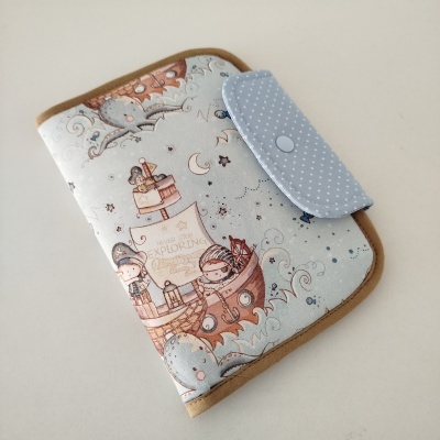 Capa de tecido ilustrada com crianças num barco e fecho azul com bolinhas brancas