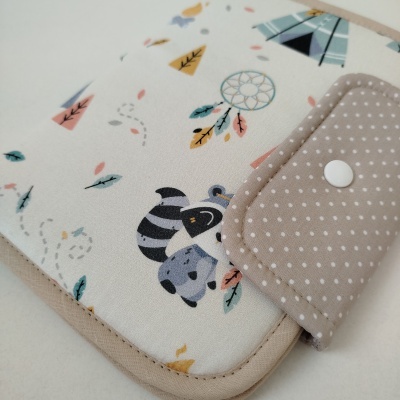 Capa de tecido branco com guaxinim e padrão de penas coloridas, fecho bege com pontos brancos