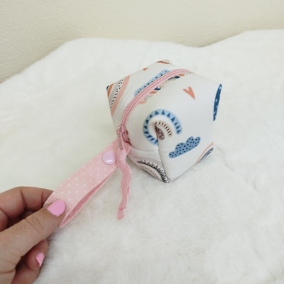 Bolsa pequena quadrada com padrão colorido e fecho rosa numa superfície branca felpuda