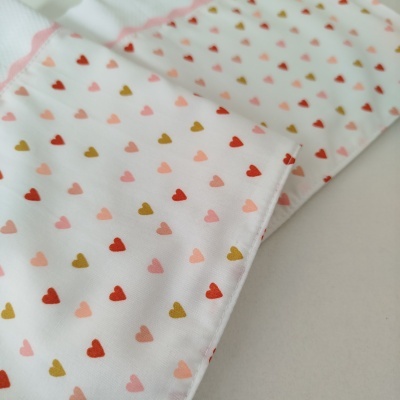 Tecido branco com padrão de corações coloridos e costura rosa ondulada.