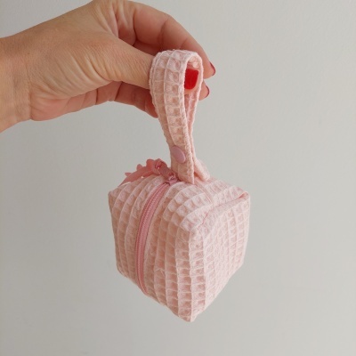 Mala pequena cor-de-rosa com padrão em relevo xadrez e alça segurada por uma mão.