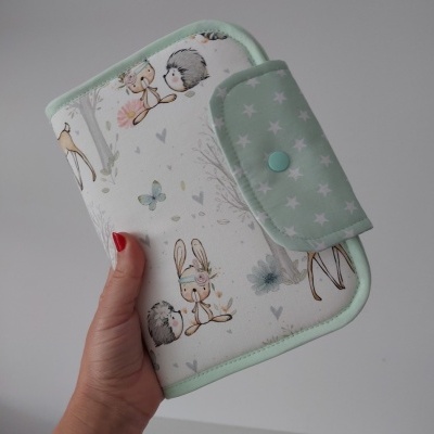 Carteira verde claro com estrelas brancas e ilustrações de animais, segurada por mão