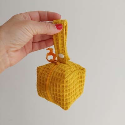 Bolsa pequena em tecido amarelo texturizado segurada por uma mão com unhas vermelhas.