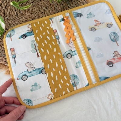 Carteira de tecido branca com padrão de carros e animais coloridos, detalhes mostarda, fechada parcialmente