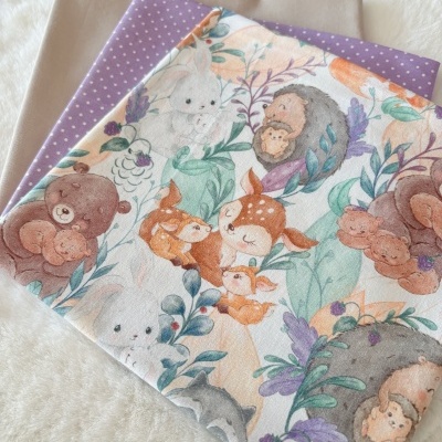 Tecidos dobrados com padrões em tons bege, lilás e ilustrações de animais e plantas