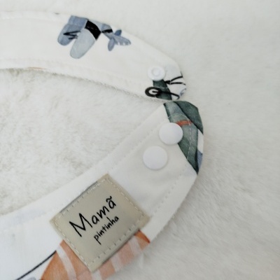 Babete branco com estampado e etiqueta 'Mamã pintinha' em tecido sobre superfície branca