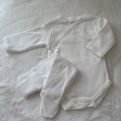 Roupa de bebé branca em algodão com body e calças sobre superfície macia branca