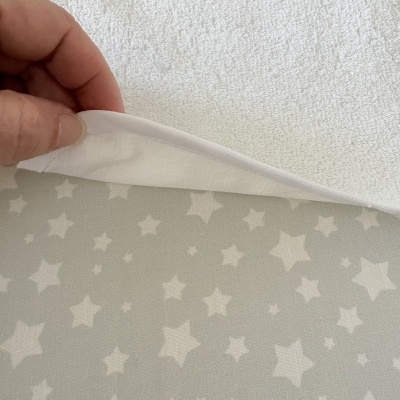 Toalha branca felpuda com barra em tecido branco sobre fundo cinzento com estrelas brancas.