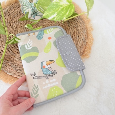 Estojo tecido com padrão de pássaro e folhas sobre superfície branca com tapete de palha