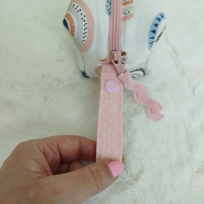 Estojo branco com padrão colorido e fecho rosa sobre superfície branca felpuda