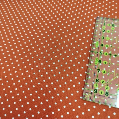 Tecido laranja com padrão de pontos brancos e régua transparente verde.