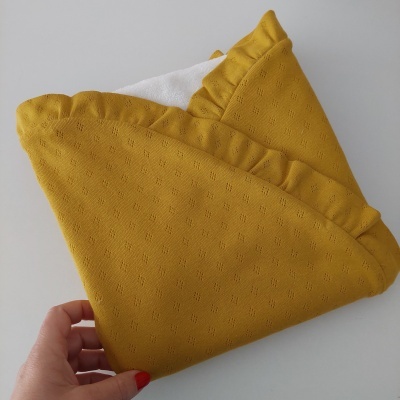 Manta ou toalha para bebé amarela com folhos e forro branco, segurada por mão.