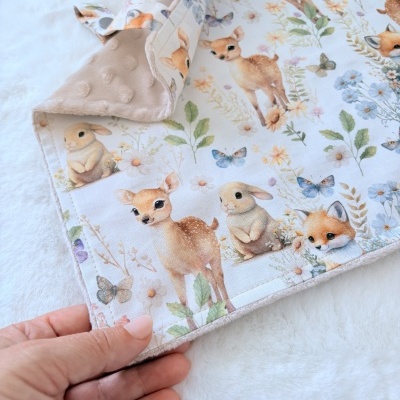 Manta para bebé com padrão de veados, coelhos e raposas em fundo branco com tecido suave bege.