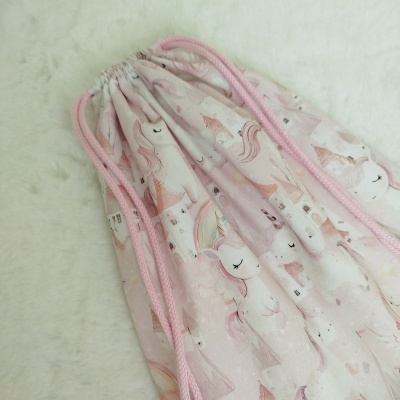 Mochila rosa claro com padrão de unicórnios e castelos sobre fundo branco